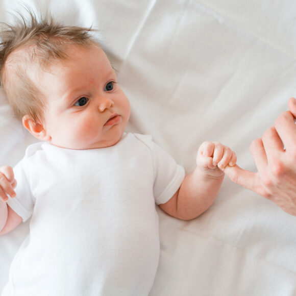 a_baby-lying-and-holding-little-finger-of-father